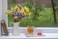 Old book, colorful bouquet of flowers and white cup of tea on background of window with raindrops at home at summer day Royalty Free Stock Photo