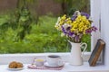 Old book, colorful bouquet of flowers and white cup of tea on background of window with raindrops at home at summer day Royalty Free Stock Photo