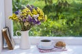 Old book, colorful bouquet of flowers and white cup of tea on background of window with raindrops at home at summer day Royalty Free Stock Photo