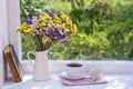 Old book, colorful bouquet of flowers and white cup of tea on background of window with raindrops at home at summer day Royalty Free Stock Photo