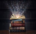 Old book with flying letters and magic light on the background of the bookshelf in the library. Ancient books as a symbol of Royalty Free Stock Photo