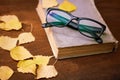 Old book, glasses and yellow autumn leaves on a wooden table Royalty Free Stock Photo