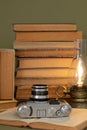 Old books, an analog camera and a stylized lamp on an olive green background