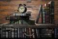 Stack of old books with alarm clock on vintage wooden wall background Royalty Free Stock Photo