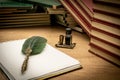 Old books stacked in disarray, an old pen with its ink and a notepad on an old wooden table and dim lighting. Selective focus. Royalty Free Stock Photo