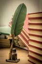 Old books stacked in disarray, an old pen with its ink and a notepad on an old wooden table and dim lighting. Selective focus. Royalty Free Stock Photo
