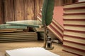 Old books stacked in disarray, an old pen with its ink and a notepad on an old wooden table and dim lighting. Selective focus. Royalty Free Stock Photo