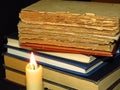 Old books stacked in a pile and a burning candle. Education, knowledge, reading habits, paper, library, light, flame, mystery.