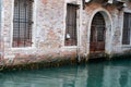 Old brick building with security protected window and door alongside and reflected in green water of canal Royalty Free Stock Photo