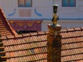 Old brick and cast iron chimney above light brown clay tile roof ridge and blurred eclectic stucco facade background