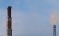 Old brick chimney on background of smoky sky and modern steaming pipe Royalty Free Stock Photo