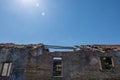 Old brick and concrete worn abandoned house with blue sky and sun on the background