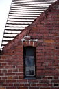 Old brick wall with a narrow window and tiled roof behind it Royalty Free Stock Photo