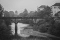 Old bridge over the river on rainy day, monochrome. Arched bridge over canal, black and white. Cloudy day in medieval village. Royalty Free Stock Photo
