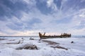 Old broken boat wreck and rocky beach in wintertime. Frozen sea, evening light and icy weather on shore like fairy tale country. Royalty Free Stock Photo