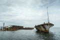 Old broken boat wreck on the shore, blue sea and sailboat on background. Royalty Free Stock Photo