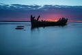 Old broken boat wreck on the shore, a frozen sea and beautiful blue sunset background. Royalty Free Stock Photo