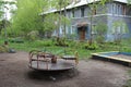 Old broken children`s carousel abandoned in the yard near the house in the grass in the summer