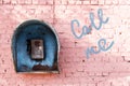 Old broken phone of the Soviet period on the pink brick wall of the house and the inscription: call me. Royalty Free Stock Photo