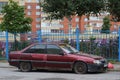 An old broken rusty abandoned dark red car stands near the blue fence Royalty Free Stock Photo