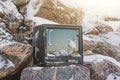 Old broken TV on the rocks in winter in the snow.