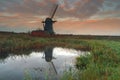 Derelict broken windmill at sunrise reflected in small pond