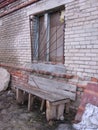 old broken window with broken glass in a ruined abandoned brick house behind bars near a wooden bench Royalty Free Stock Photo