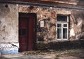 Old broken wooden brown door with handle in aged dirty plaster old town building with white painted frame wooden window Royalty Free Stock Photo