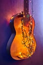 Old broken wooden guitar decorated bright glowing garland. Musical instrument hanging on wall. Christmas interior decoration. Royalty Free Stock Photo