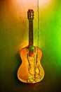 Old broken wooden guitar decorated bright green glowing garland. Musical instrument hanging on wall. Christmas interior Royalty Free Stock Photo