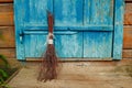 An old broom on the background of a blue antique wooden door