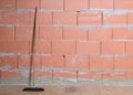 Old broom is leaning against a raw brick wall from Porotherm style clay blocks in a house under construction, architecture