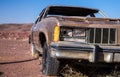 Old brown car with a busted headlight and flat tire in the desert under a blue sky