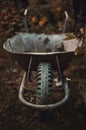 Old And Brown Garden Wheelbarrow Filled With Grass And Dirty Lops With Blurred Background. Vertical Photo Of Half Empty And Rusty
