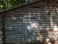 Old brown and grey farm shed with rusted wheel on the outside wall in the forest