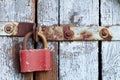 Old brown padlock on a gray door with wooden planks of cracked paint and rust. Vintage gates with metal stripes and bolts Royalty Free Stock Photo