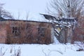 Old brown ruined brick house with empty black windows in white snow overgrown with plants and trees Royalty Free Stock Photo