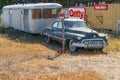 Old Buick sedan hitched to caravan parked and left besideprivate property sign with signs of known brands on fence