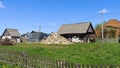 An old building, a wooden barn with a slate roof, stands on a grassy lawn with dandelions in a rural setting. Behind the old board