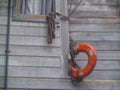 Old buoy hanging by rope on side of weathered timber wall