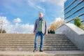 Old businessman in stylish scarf stand on paved stairs on blue sky background, from below view. Man walk outdoors. Royalty Free Stock Photo