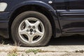 An old car with a flat or deflated tire. A sedan parked by a concrete road on a hot day