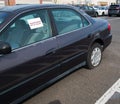 Old car with flat tire in parking lot with sticker on window that says Abandoned