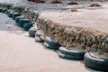 Old car tires used as for strengthening concrete sidewalk area built on sandy beach at high tide water level, perspective view