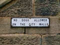 An old cast iron black and white sign fixed to a sandstone walls advises that no dogs are allowed on the City walls in York,