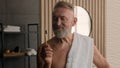 Old Caucasian retired male senior man with bath towel on shoulder showing holding bamboo tooth brush recommend brushing