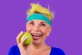 Old caucasian snow-white smile woman with short yellow dyed hair and a blue bandage on forehead eating green fresh apple