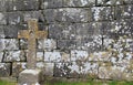 Old Celtic cross leaning against moss and lichen covered stone wall