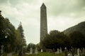 Old cemetery with round tower in Glendalough monastic site with stone wall, mountains and forest in the background, Ireland.