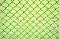 Old chain link pattern abstract fence with green grass field background. Focus foreground with soft, blurry background.